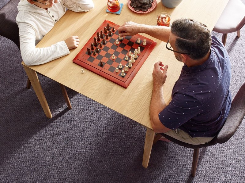 Father and son playing chess at a wooden table in a room with purple carpet from Simonian Flooring Inc in Village, NV