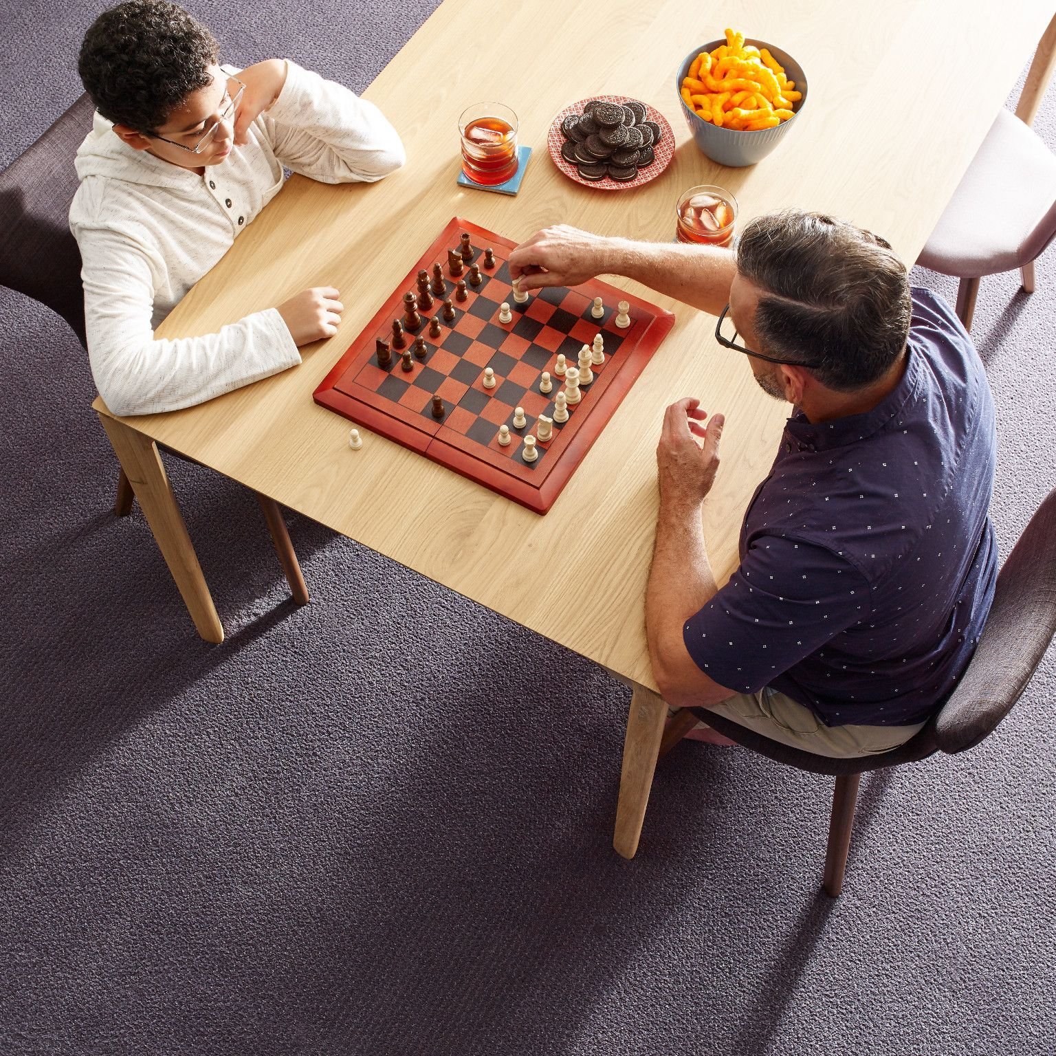 Father and son playing chess at a wooden table in a room with purple carpet from Simonian Flooring Inc in Village, NV